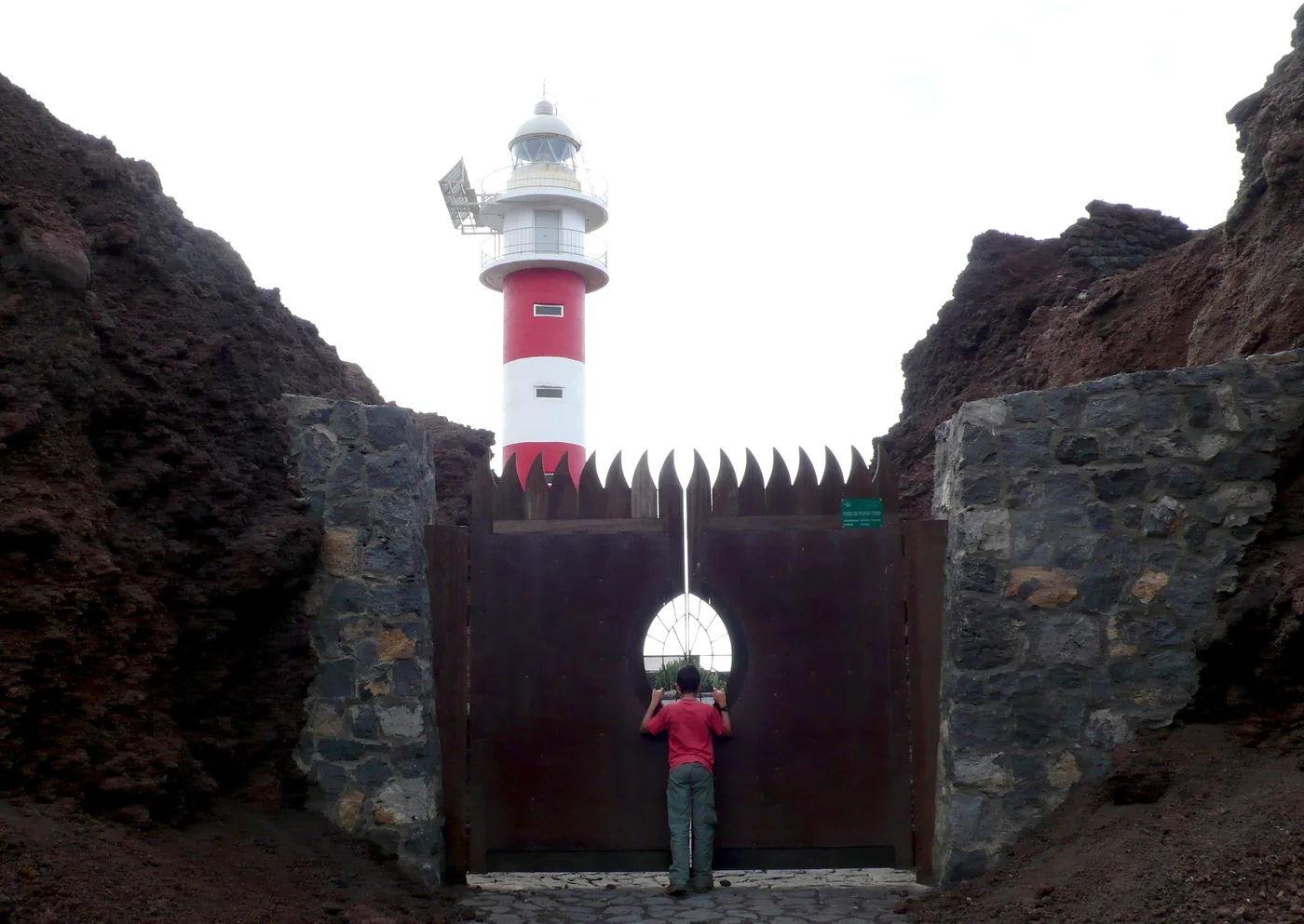 The red-and-white lighthouse of Punta de Teno behind a gate between dark rock walls, Tenerife.